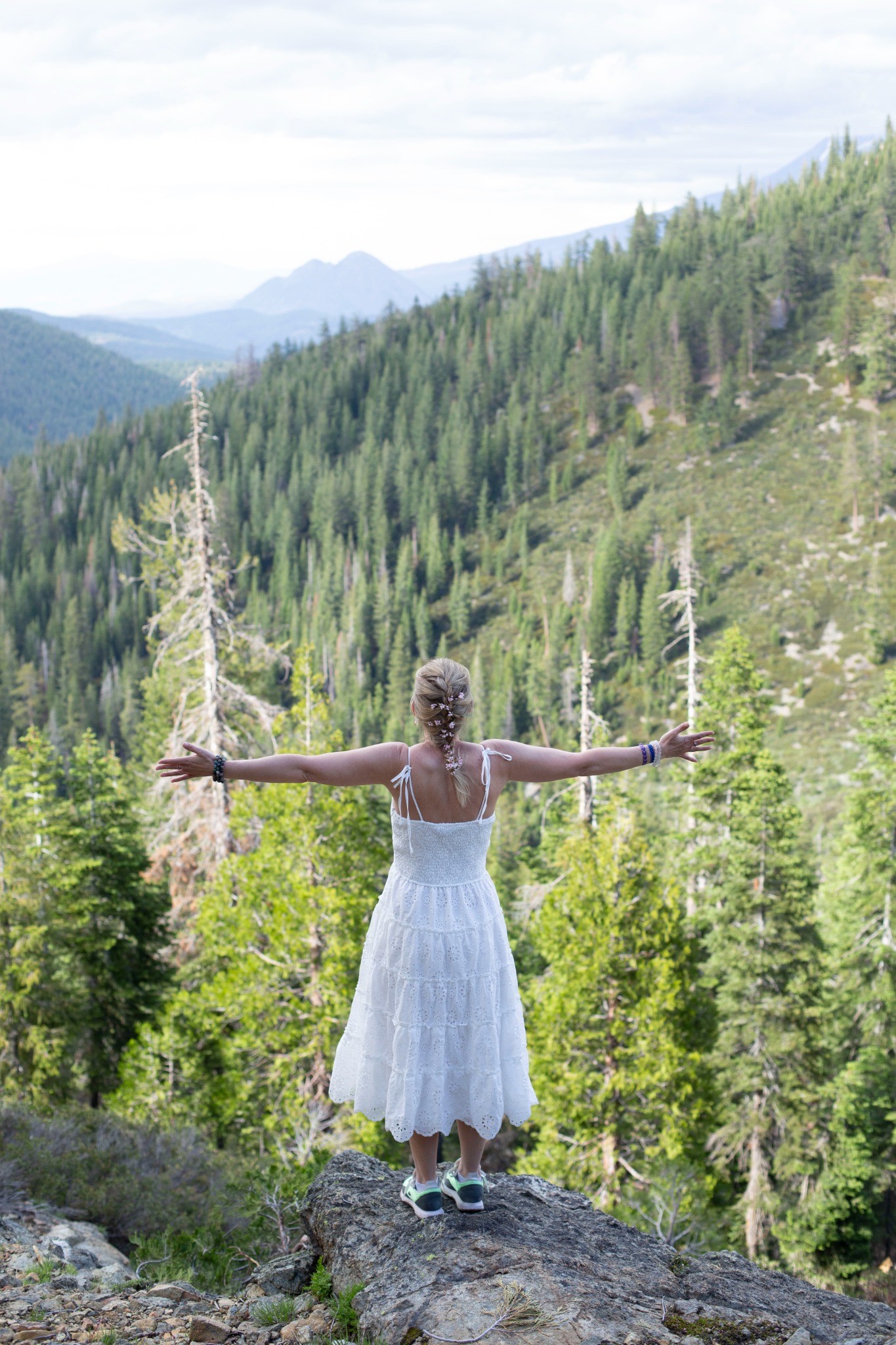 Irina standing with open arms above a wide forested mountain landscape